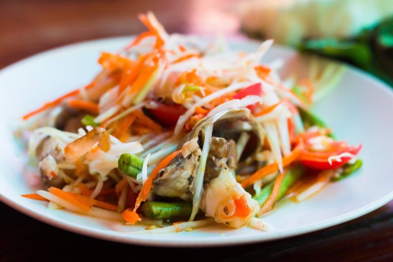Close-up of a vibrant Thai papaya salad with fresh vegetables and herbs.