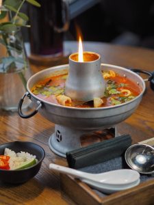 A savory Tom Yum soup served in a flaming hot pot, perfect for a cozy meal.