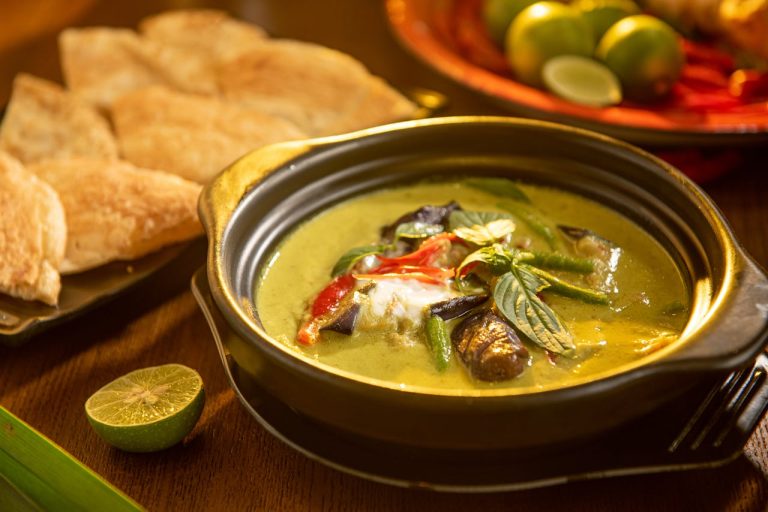 A flavorful Thai green curry with vegetables and aromatic herbs in a stylish black bowl.